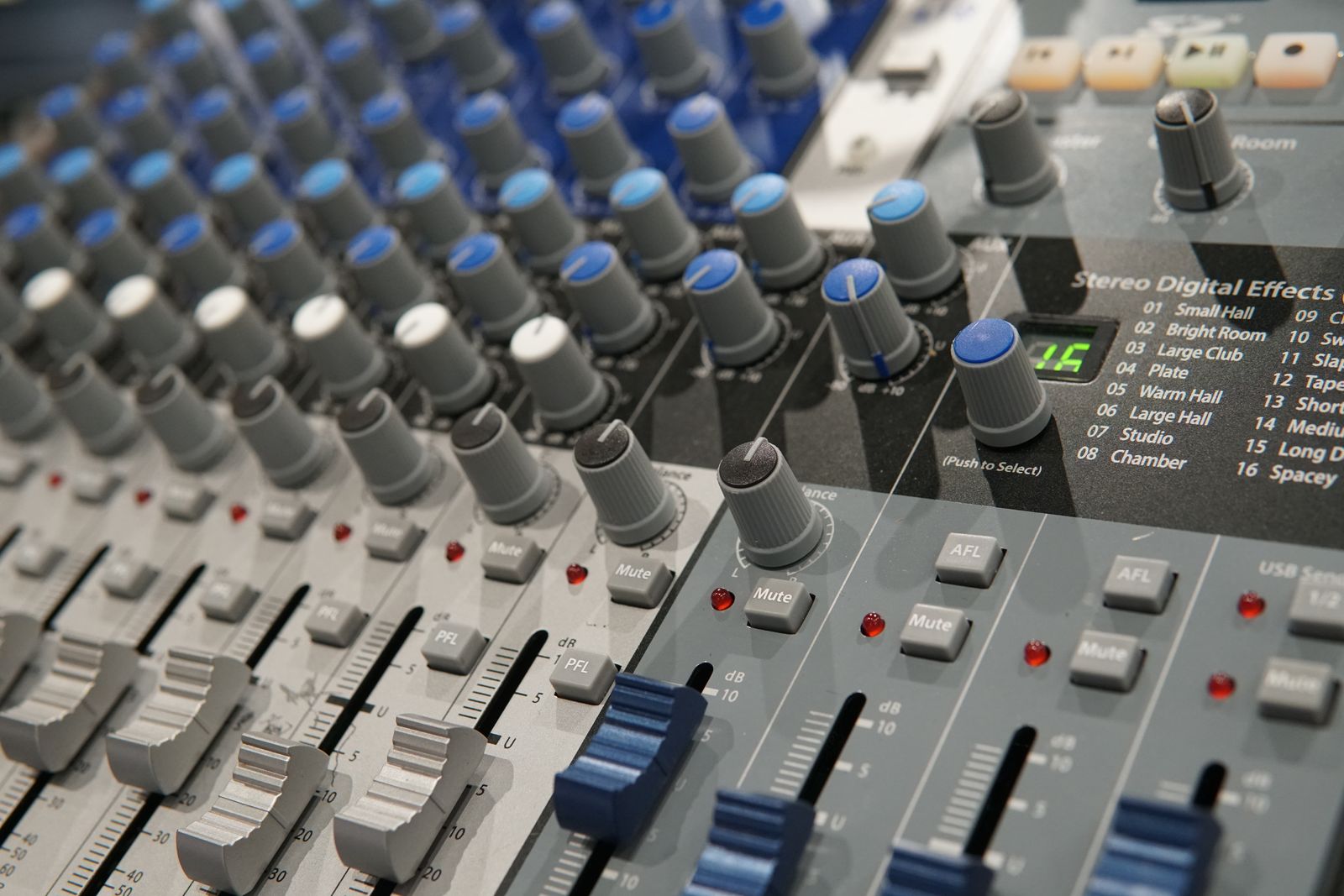 Detalhe de console de áudio com controles e faders; imagem de referência.